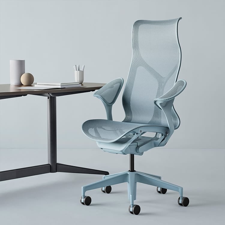 A sleek, light blue Herman Miller Cosm ergonomic chair with a breathable mesh back and seat sits gracefully next to a minimalist desk adorned with essential office supplies, all set against a soft gray backdrop. Studio Office Cyprus
