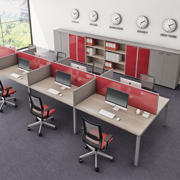 A sleek I-Work Operative office showcasing six contemporary workstations accented by bold red dividers, paired with black and red chairs. Each desk features a computer, while wall-mounted cabinets above display clocks set to different world time zones. Studio Office Cyprus