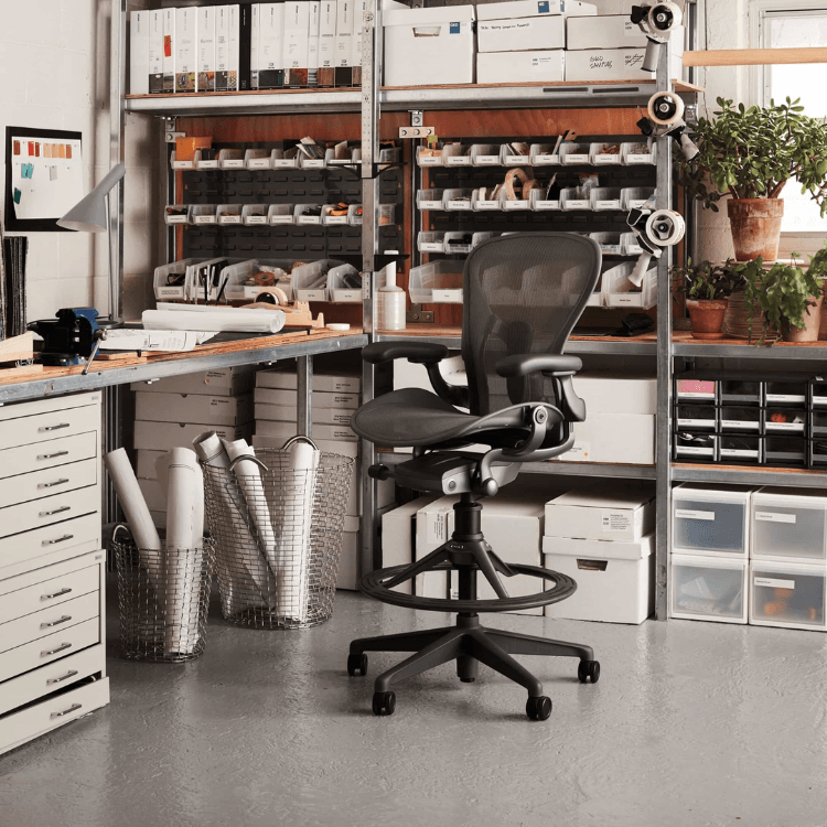 Ergonomic black Aeron Stool with mesh back, adjustable arms, and footrest in a workshop setting.