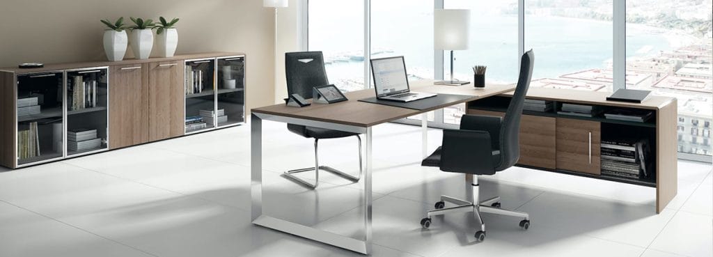 Modern office setup with GENESIS executive desk, black chairs, wood cabinets, and large windows.