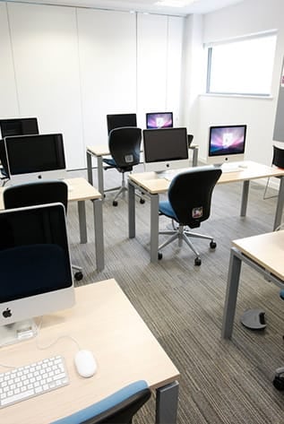 Higher Education computer lab featuring desks, chairs, and Apple computers.
