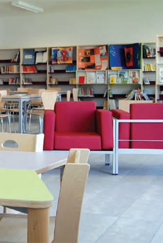 Modern library furniture: red chairs, light wood tables, and bookshelves.
