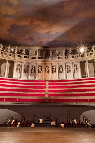 Elegant theater interior with red seating, statues, and a painted sky ceiling.