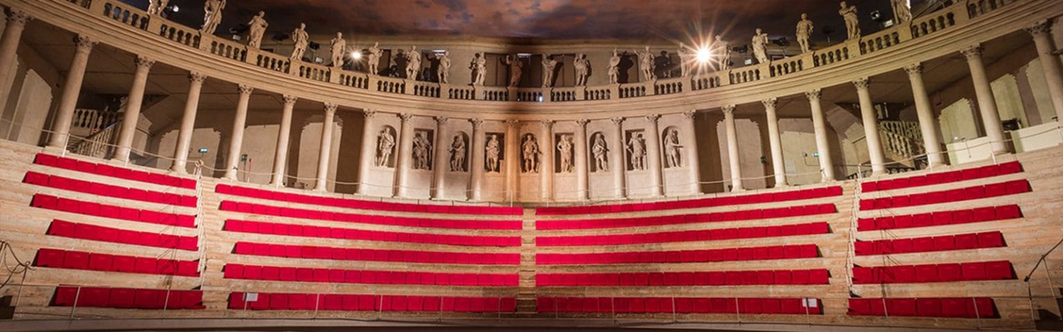 Classical theater seating with red cushioned benches and stone architecture.