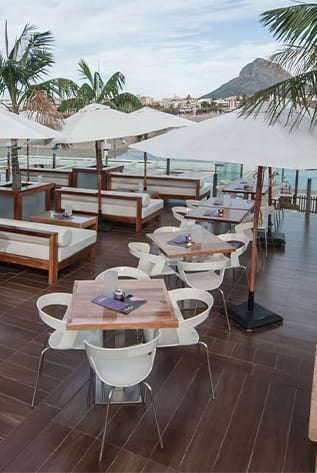 Hotel patio furniture: tables, chairs, and lounge seating under white umbrellas.