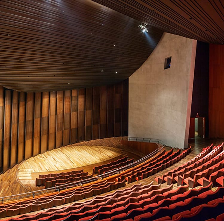 Elegant theater interior with red seating, wood stage, and modern design.