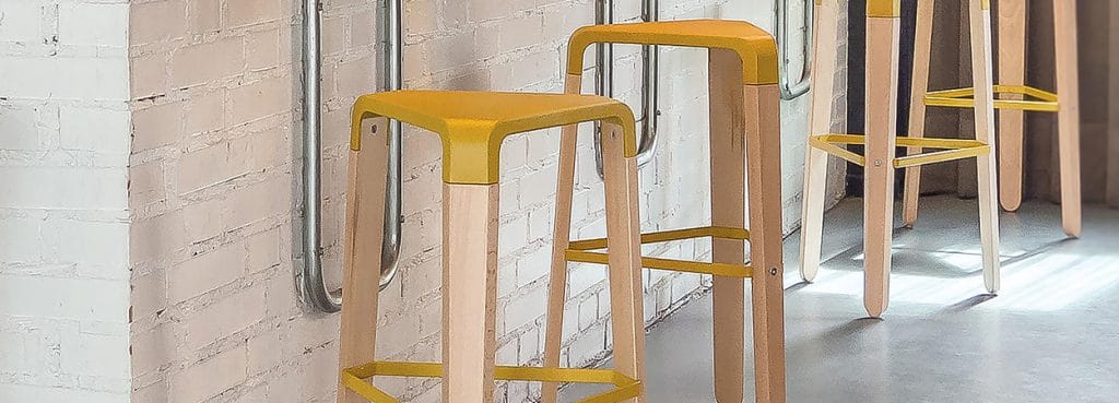 Angled view of yellow Picapau Stool with light wood legs and triangular footrest.