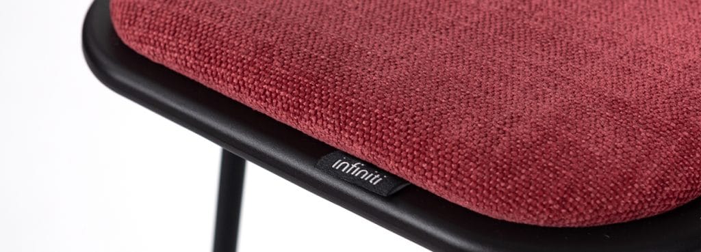 Close-up of a Klejn Stool with a red fabric seat and black frame. Modern, minimalist design for social spaces.