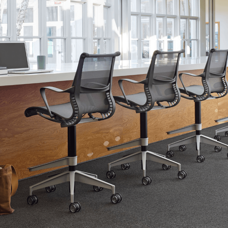 Angled view of gray Herman Miller Setu Stool with mesh back and seat, on casters.