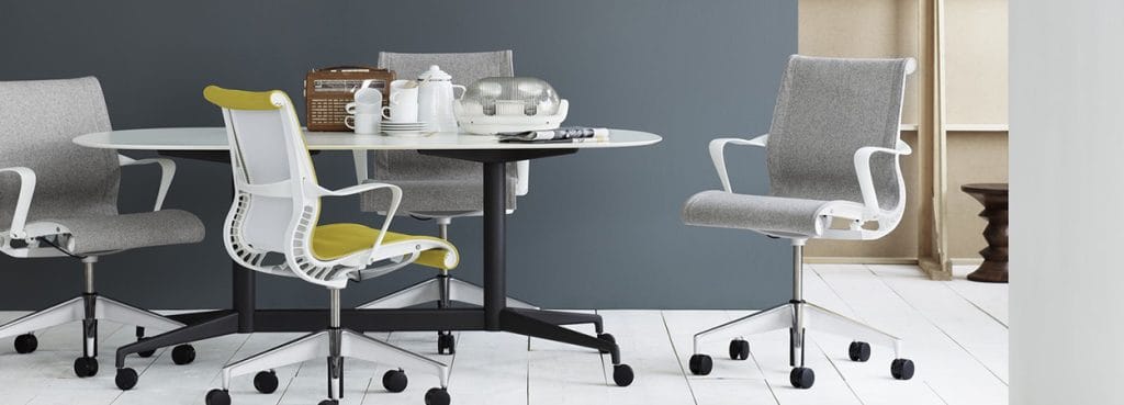 Modern Setu Visitor Chair in gray and yellow with a white frame, around a white table with black legs.