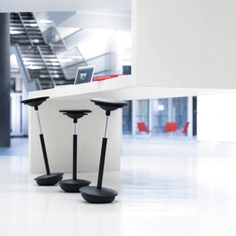 Three black Stitz 2 perching stools in a modern, bright office space.