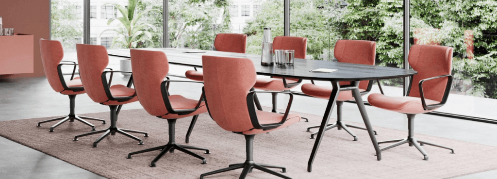 Modern Versa Conference Table with coral chairs in a bright meeting room, angled view.