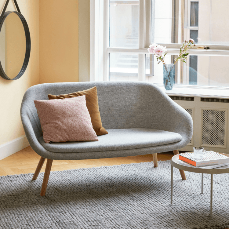 Modern gray AAL Sofa with wood legs, pink and brown pillows. Stylish, comfortable seating for social spaces.