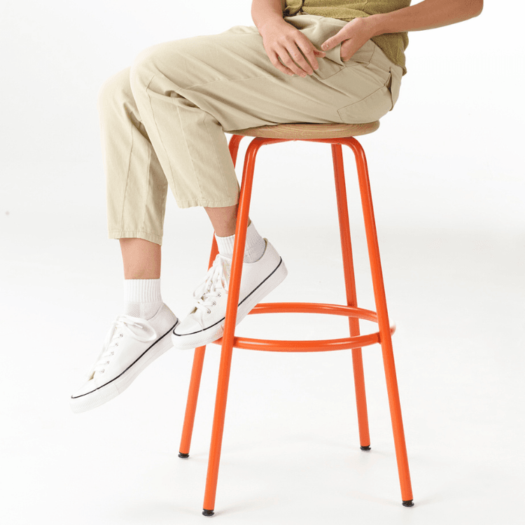 Person sitting on a bright orange Penny Stool with a wooden seat.