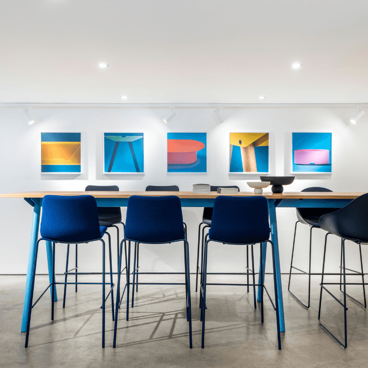 Modern interior featuring NaughtOne's Ruby Stool. Blue stools line a table against a white wall with colorful art.