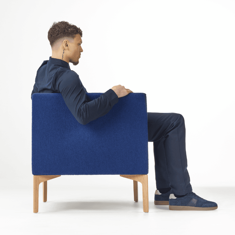 Side view of a man sitting in a blue Symbol Lounge Chair with wood legs.