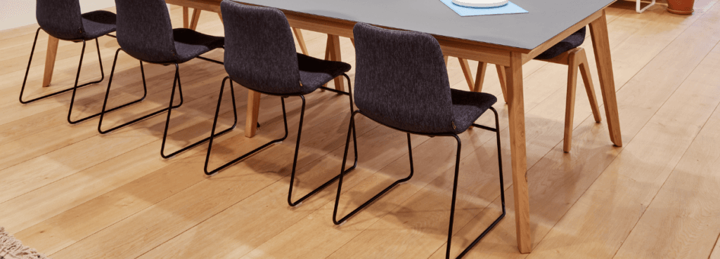 Upholstered Viv Side Chair with black sled base, next to a wooden table.
