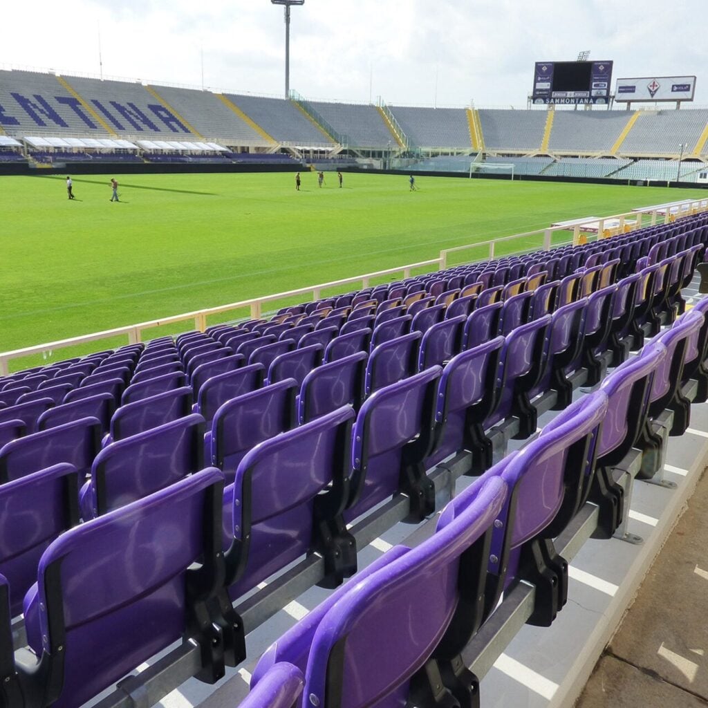 Purple tip-up stadium seats in long rows beside a pitch